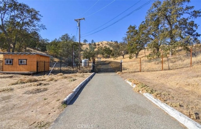 view of road with a rural view, curbs, a gated entry, and a gate