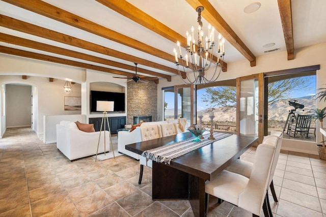 dining area with ceiling fan with notable chandelier, beamed ceiling, and a fireplace