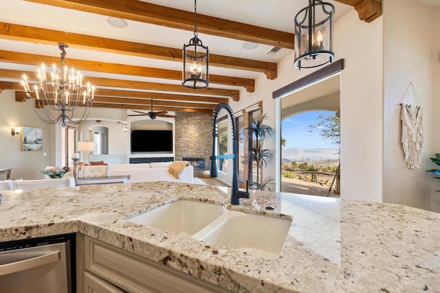 kitchen with a stone fireplace, beamed ceiling, decorative light fixtures, dishwasher, and sink