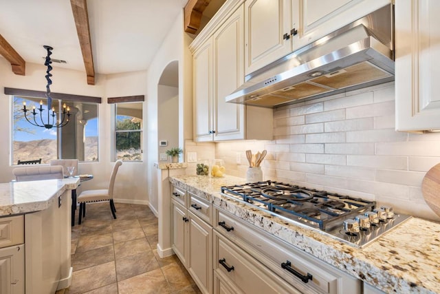 kitchen featuring an inviting chandelier, tasteful backsplash, stainless steel gas cooktop, pendant lighting, and beamed ceiling