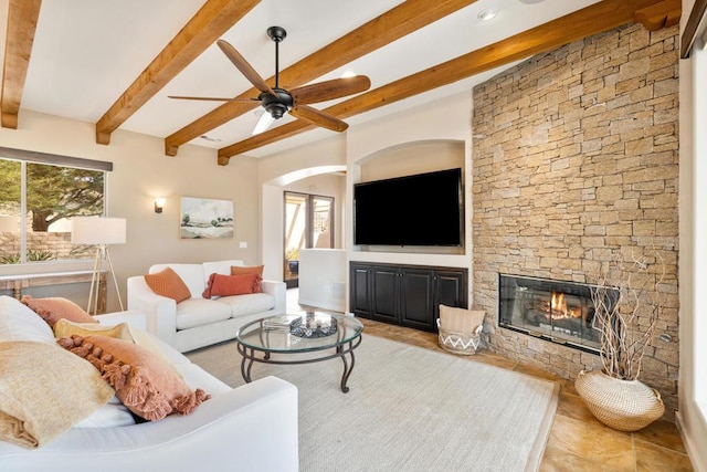 living room with ceiling fan, beamed ceiling, and a fireplace