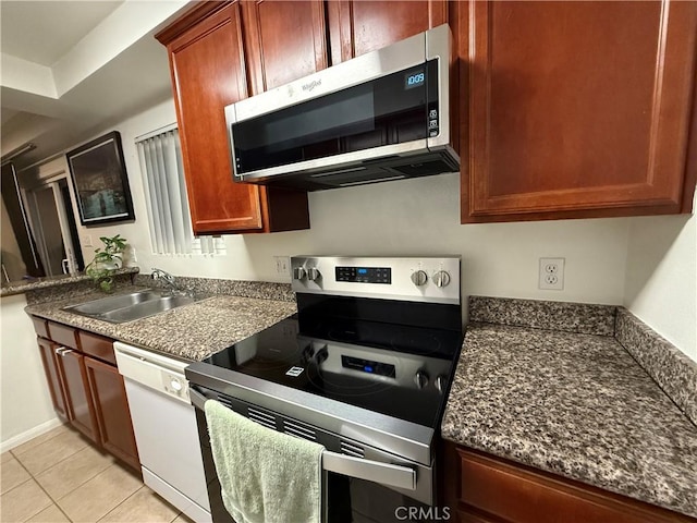 kitchen featuring light tile patterned floors, stainless steel appliances, a sink, and reddish brown cabinets