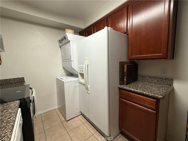 kitchen with light tile patterned flooring, stacked washer and dryer, white refrigerator with ice dispenser, baseboards, and dark countertops