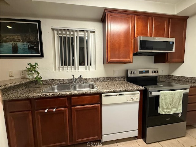 kitchen featuring light tile patterned floors, a sink, dark brown cabinets, appliances with stainless steel finishes, and dark countertops