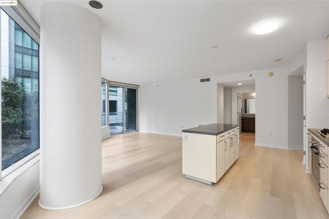 kitchen featuring white cabinetry, a wall of windows, a kitchen island, and light wood-type flooring