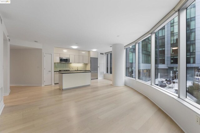 interior space with white cabinets, backsplash, appliances with stainless steel finishes, and light hardwood / wood-style flooring