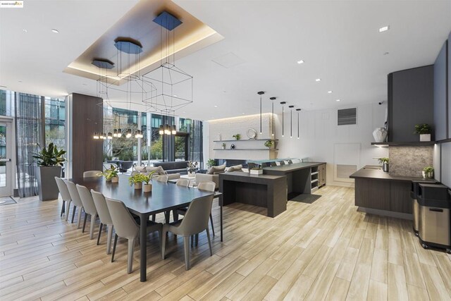 dining area featuring a wall of windows, an inviting chandelier, a tray ceiling, and light hardwood / wood-style flooring