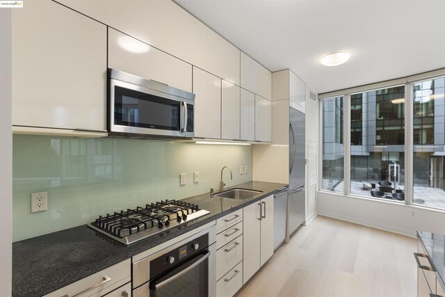 kitchen featuring dark stone countertops, light hardwood / wood-style floors, sink, white cabinetry, and appliances with stainless steel finishes