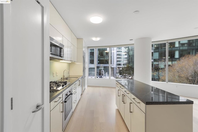 kitchen featuring light hardwood / wood-style flooring, appliances with stainless steel finishes, dark stone counters, white cabinets, and sink