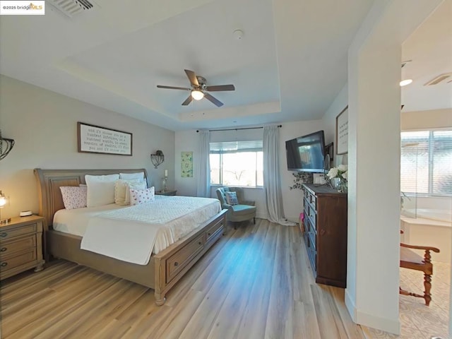 bedroom with ceiling fan, light hardwood / wood-style flooring, and a raised ceiling