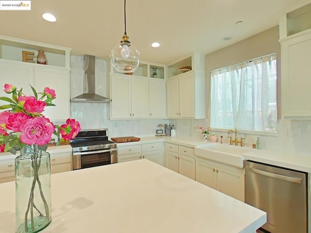 kitchen featuring white cabinetry, appliances with stainless steel finishes, decorative light fixtures, wall chimney exhaust hood, and sink