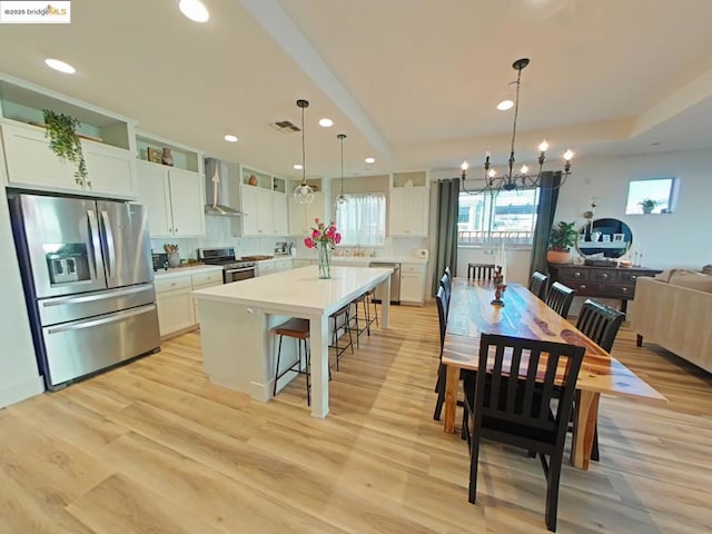 kitchen with decorative light fixtures, wall chimney range hood, a kitchen island, stainless steel appliances, and white cabinets