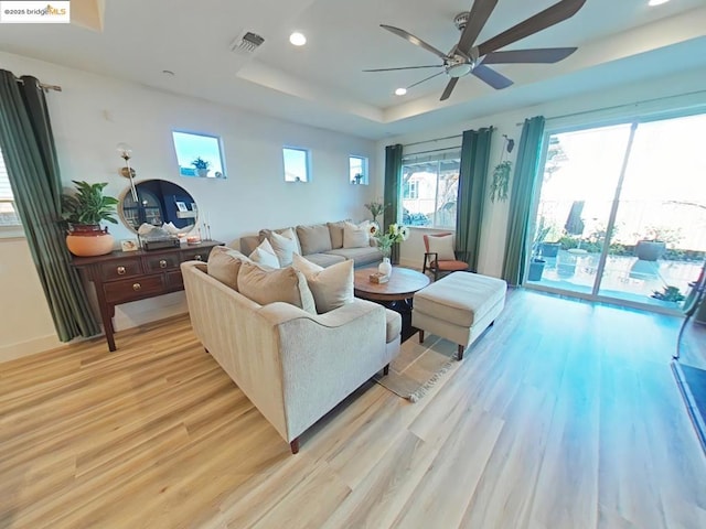 living room featuring light wood-type flooring, ceiling fan, and a tray ceiling