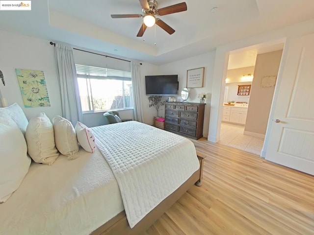 bedroom featuring ceiling fan, ensuite bathroom, light hardwood / wood-style floors, and a tray ceiling