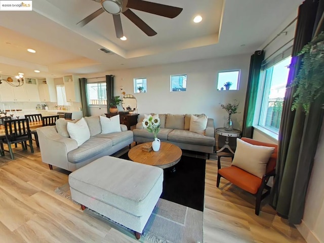 living room featuring a raised ceiling, a healthy amount of sunlight, ceiling fan, and light wood-type flooring