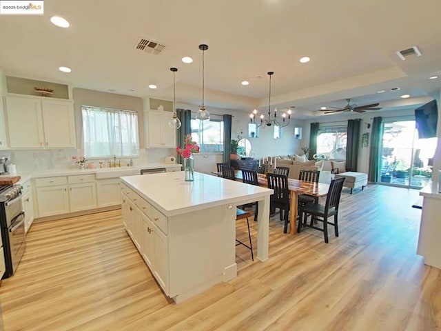 kitchen with white cabinetry, light hardwood / wood-style floors, hanging light fixtures, ceiling fan with notable chandelier, and a center island