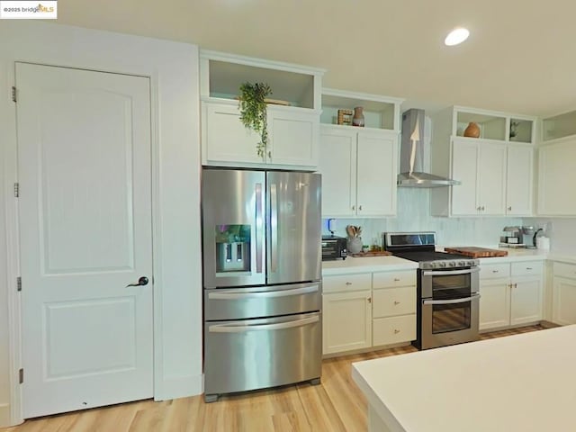 kitchen featuring light hardwood / wood-style flooring, wall chimney range hood, stainless steel appliances, and white cabinetry