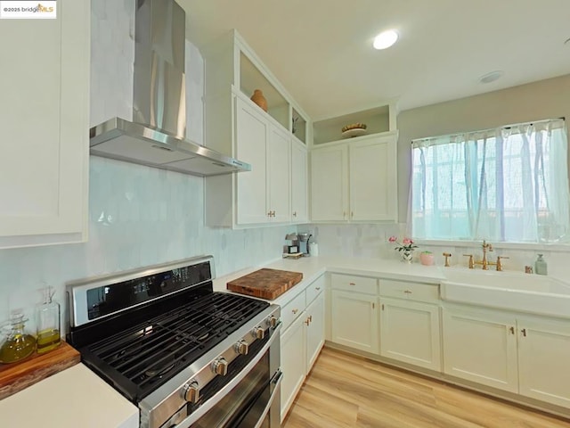 kitchen featuring stainless steel range, white cabinets, wall chimney exhaust hood, light hardwood / wood-style flooring, and sink