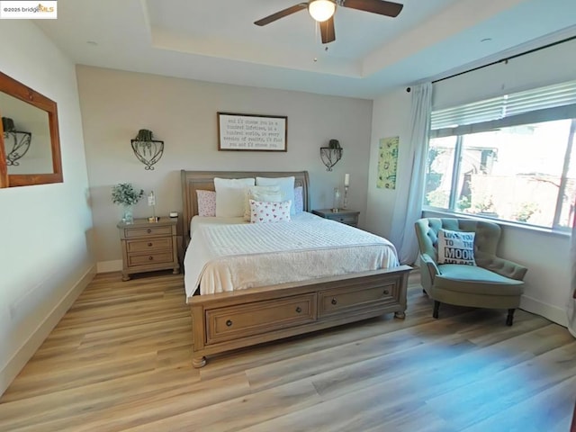 bedroom with ceiling fan, light hardwood / wood-style flooring, and a tray ceiling