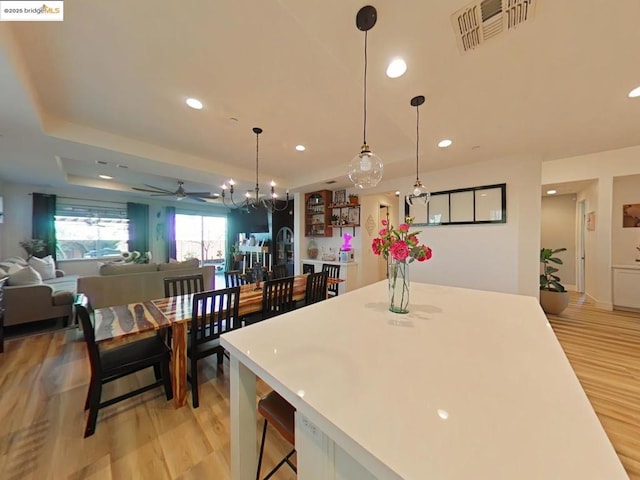 kitchen featuring ceiling fan with notable chandelier, pendant lighting, a tray ceiling, light hardwood / wood-style flooring, and a breakfast bar area