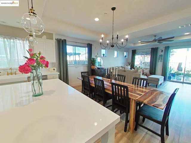 dining room with ceiling fan with notable chandelier, a wealth of natural light, and light hardwood / wood-style flooring