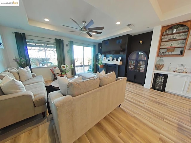 living room with light hardwood / wood-style floors, a raised ceiling, and ceiling fan