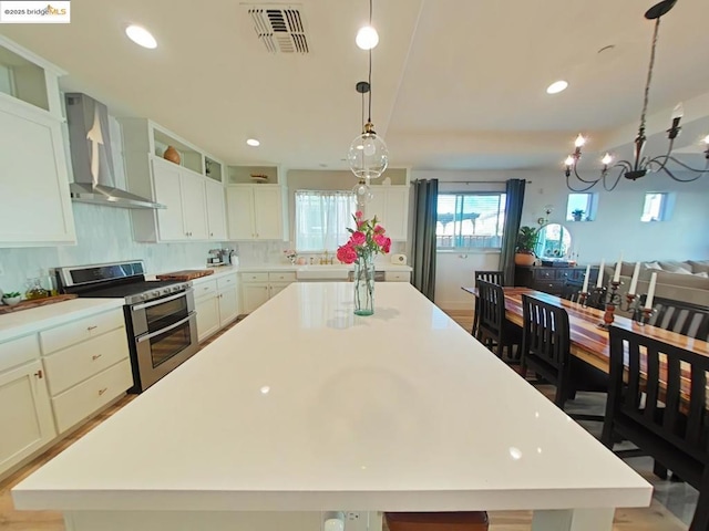 kitchen with a notable chandelier, range with two ovens, a large island, white cabinets, and wall chimney exhaust hood