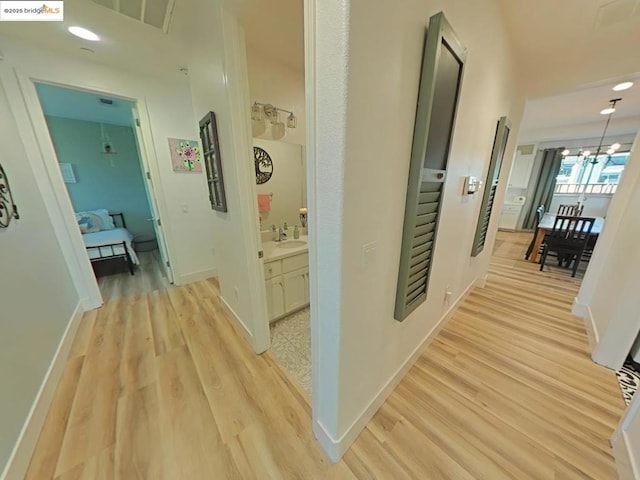 corridor featuring a notable chandelier, sink, and light hardwood / wood-style floors