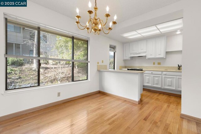 kitchen with an inviting chandelier, light wood-type flooring, hanging light fixtures, and white cabinetry