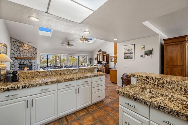 kitchen with ceiling fan, white cabinets, lofted ceiling, and a stone fireplace