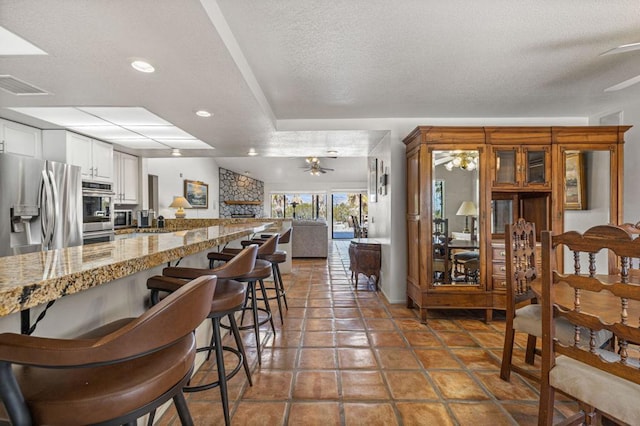 kitchen featuring light stone countertops, a textured ceiling, white cabinetry, stainless steel appliances, and a kitchen breakfast bar