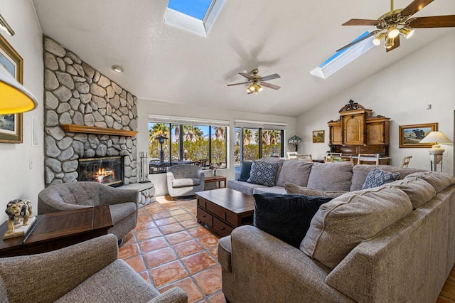 living room with ceiling fan, vaulted ceiling with skylight, light tile patterned flooring, and a fireplace