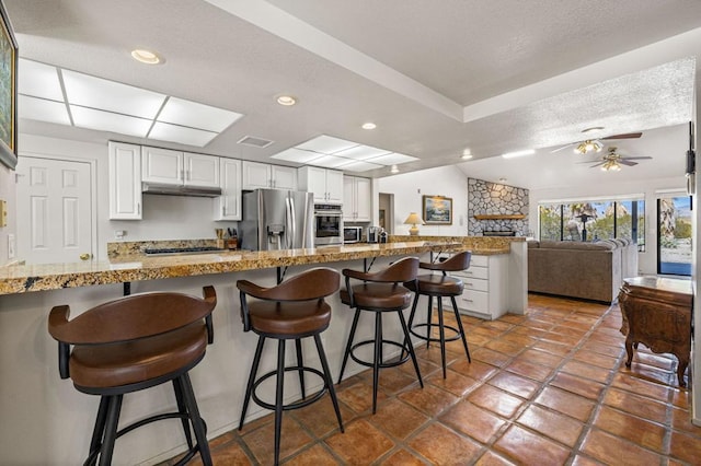 kitchen with white cabinets, stainless steel appliances, kitchen peninsula, ceiling fan, and a breakfast bar