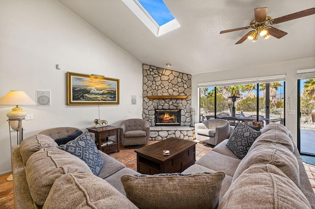 living room featuring ceiling fan, vaulted ceiling with skylight, and a fireplace