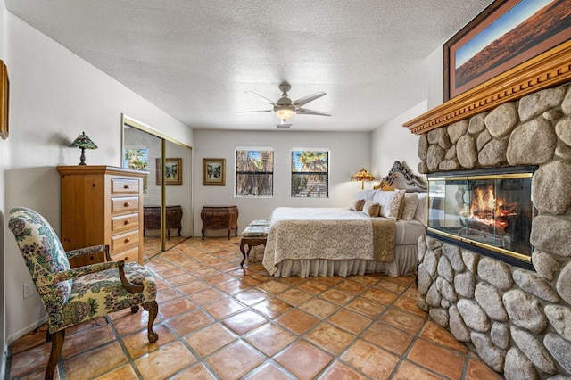 tiled bedroom with ceiling fan, a closet, a stone fireplace, and a textured ceiling