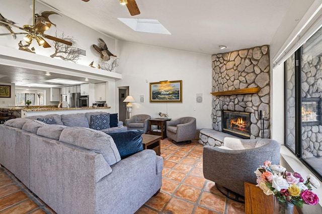 living room with ceiling fan, a skylight, a stone fireplace, and tile patterned flooring