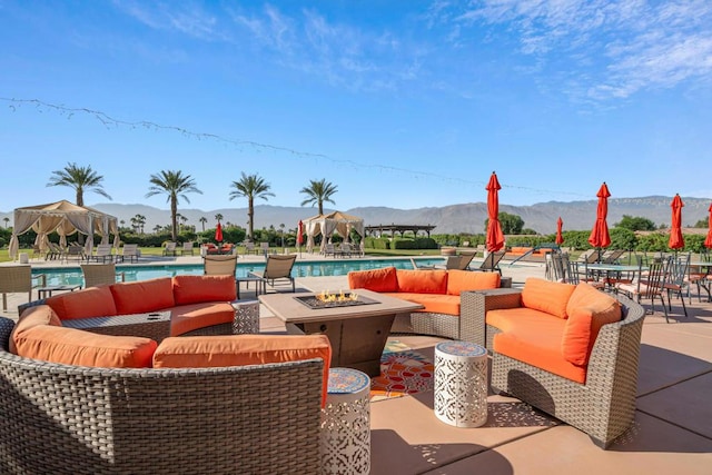 view of patio / terrace featuring a gazebo, an outdoor living space with a fire pit, a community pool, and a mountain view