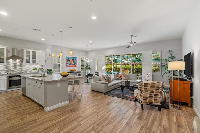 kitchen with a center island with sink, stainless steel appliances, wall chimney exhaust hood, white cabinets, and sink