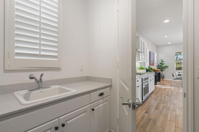 kitchen with sink, white cabinets, ventilation hood, and oven