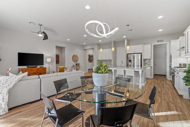 dining area featuring sink, ceiling fan with notable chandelier, and light hardwood / wood-style flooring