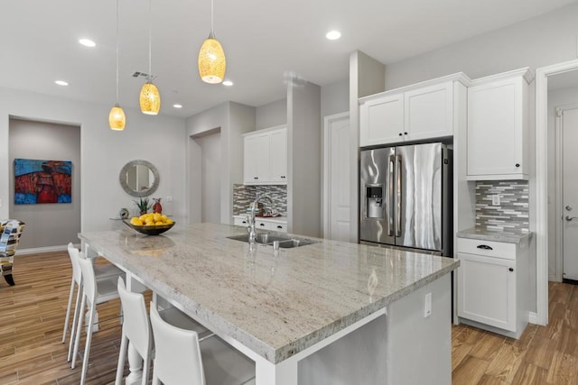 kitchen featuring white cabinetry, stainless steel fridge, decorative backsplash, a kitchen island with sink, and hanging light fixtures