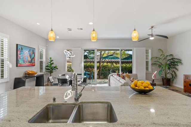 kitchen with decorative light fixtures, light stone countertops, a wealth of natural light, and sink