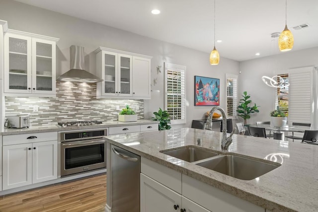 kitchen with wall chimney exhaust hood, sink, stainless steel appliances, and white cabinetry