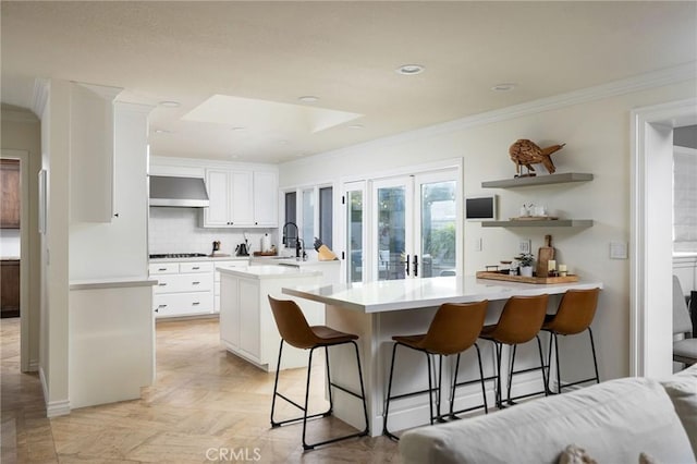 kitchen featuring white cabinetry, a breakfast bar, kitchen peninsula, and range hood