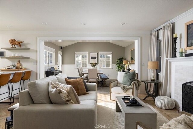 living room with vaulted ceiling, a brick fireplace, and ornamental molding