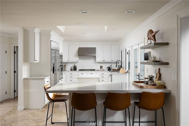 kitchen featuring exhaust hood, decorative backsplash, a kitchen breakfast bar, gas stovetop, and white cabinets