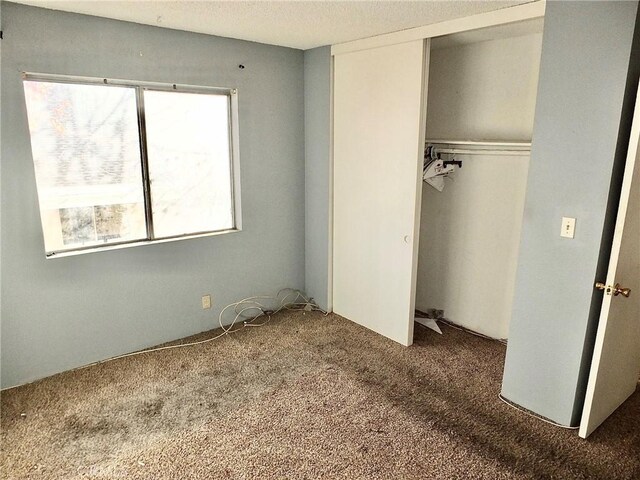 unfurnished bedroom with dark carpet and a closet