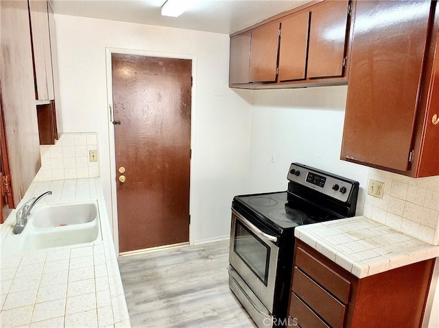 kitchen with tile countertops, light hardwood / wood-style floors, decorative backsplash, electric stove, and sink