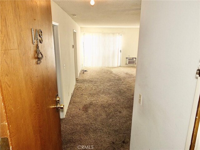 hall with an AC wall unit, carpet floors, and a textured ceiling