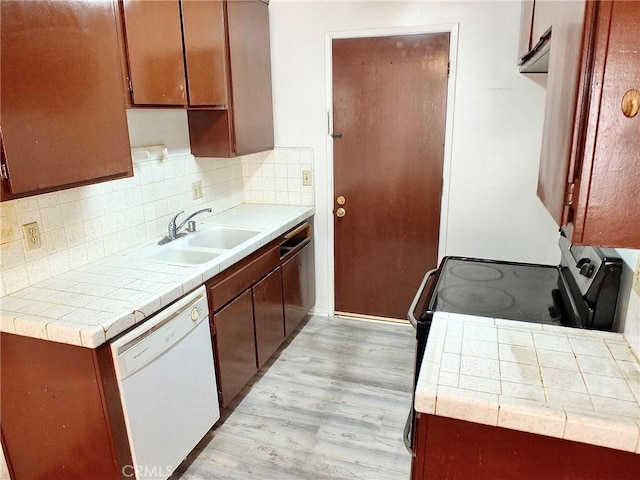 kitchen featuring backsplash, light hardwood / wood-style floors, sink, white dishwasher, and tile counters